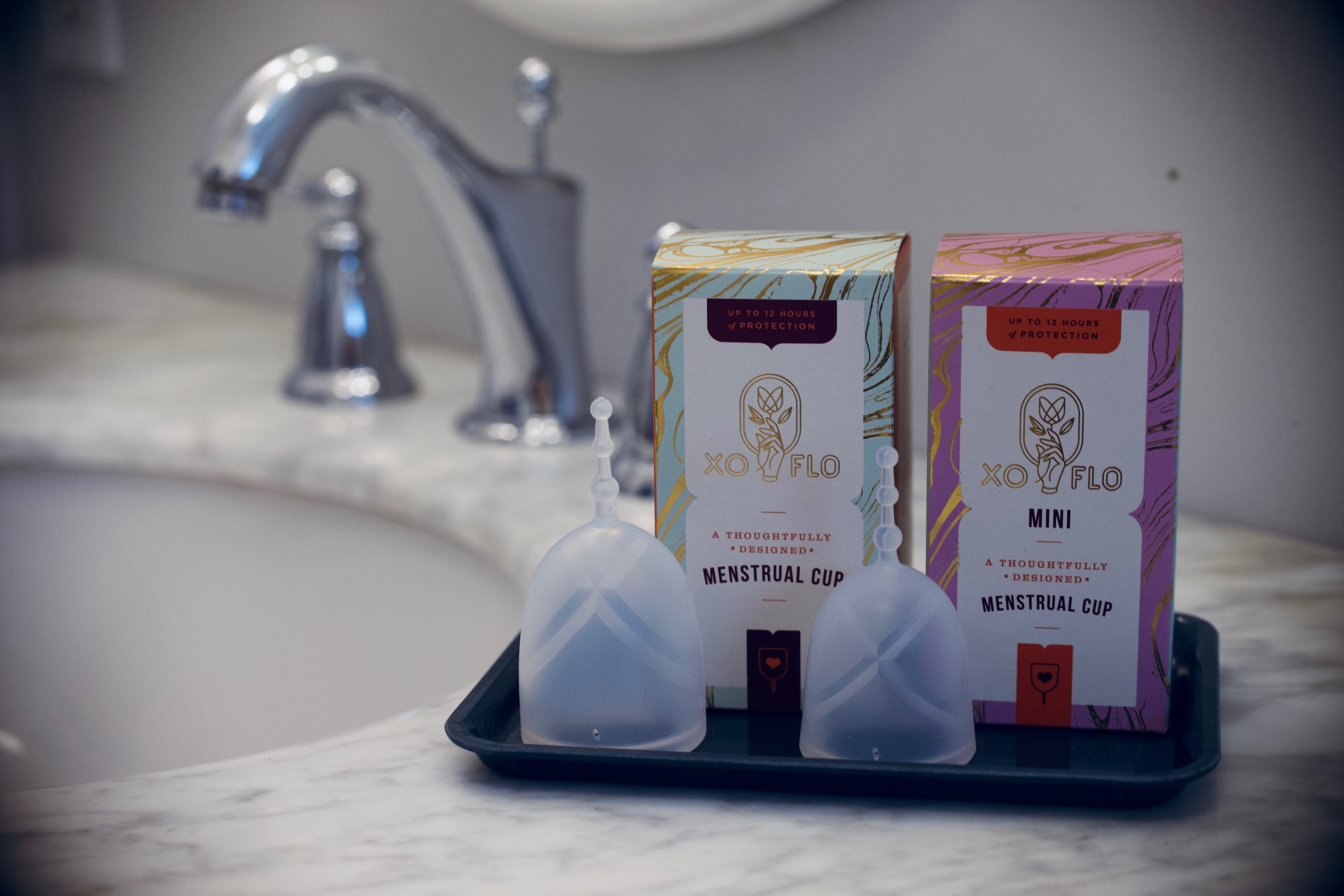 Two sizes of XO Flo menstrual cups sit on a bathroom counter.