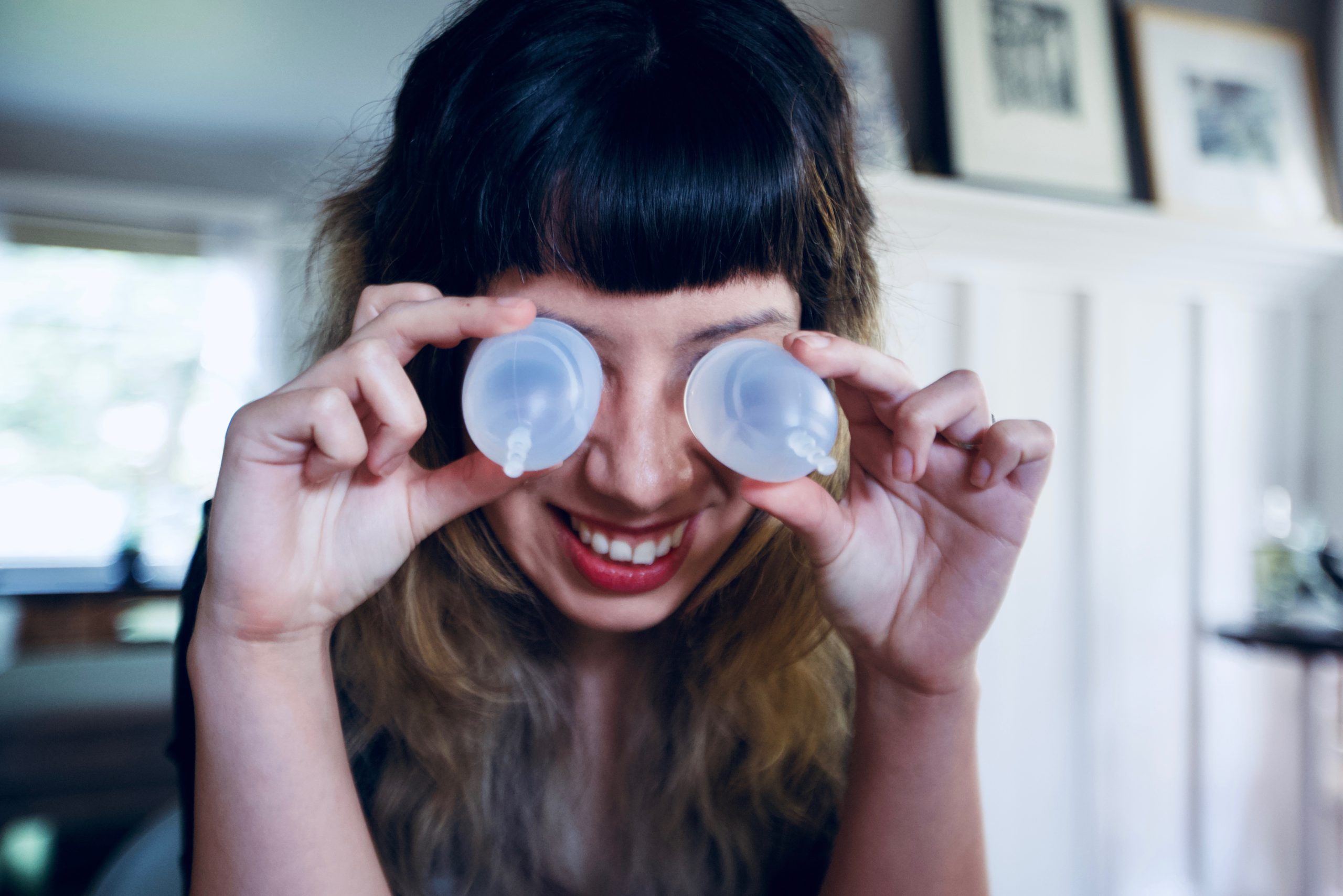 A person playfully looks through two different sized menstrual cups.