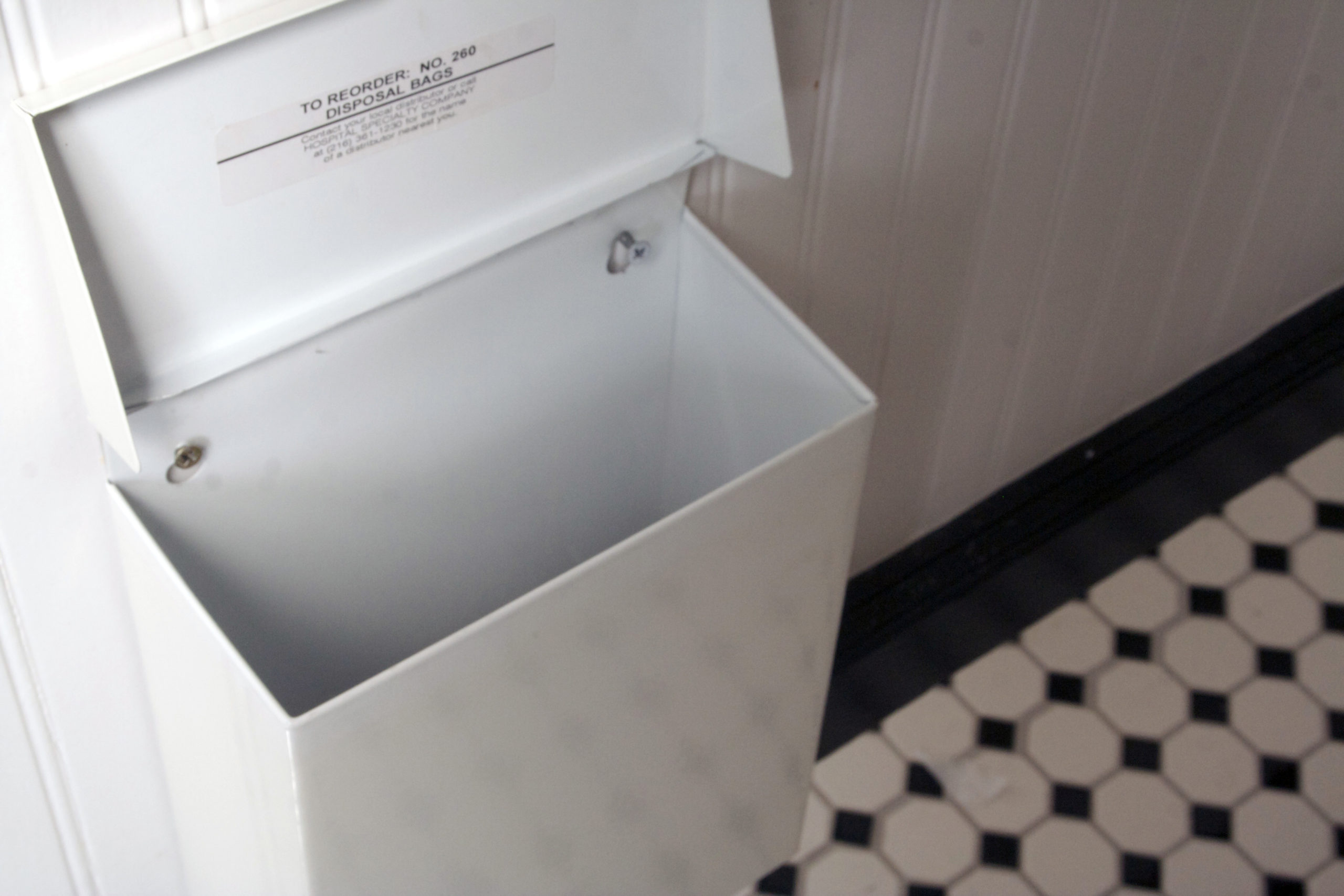 An empty bathroom stall trash can with a sticker that says "to reorder no 260 disposal bags".