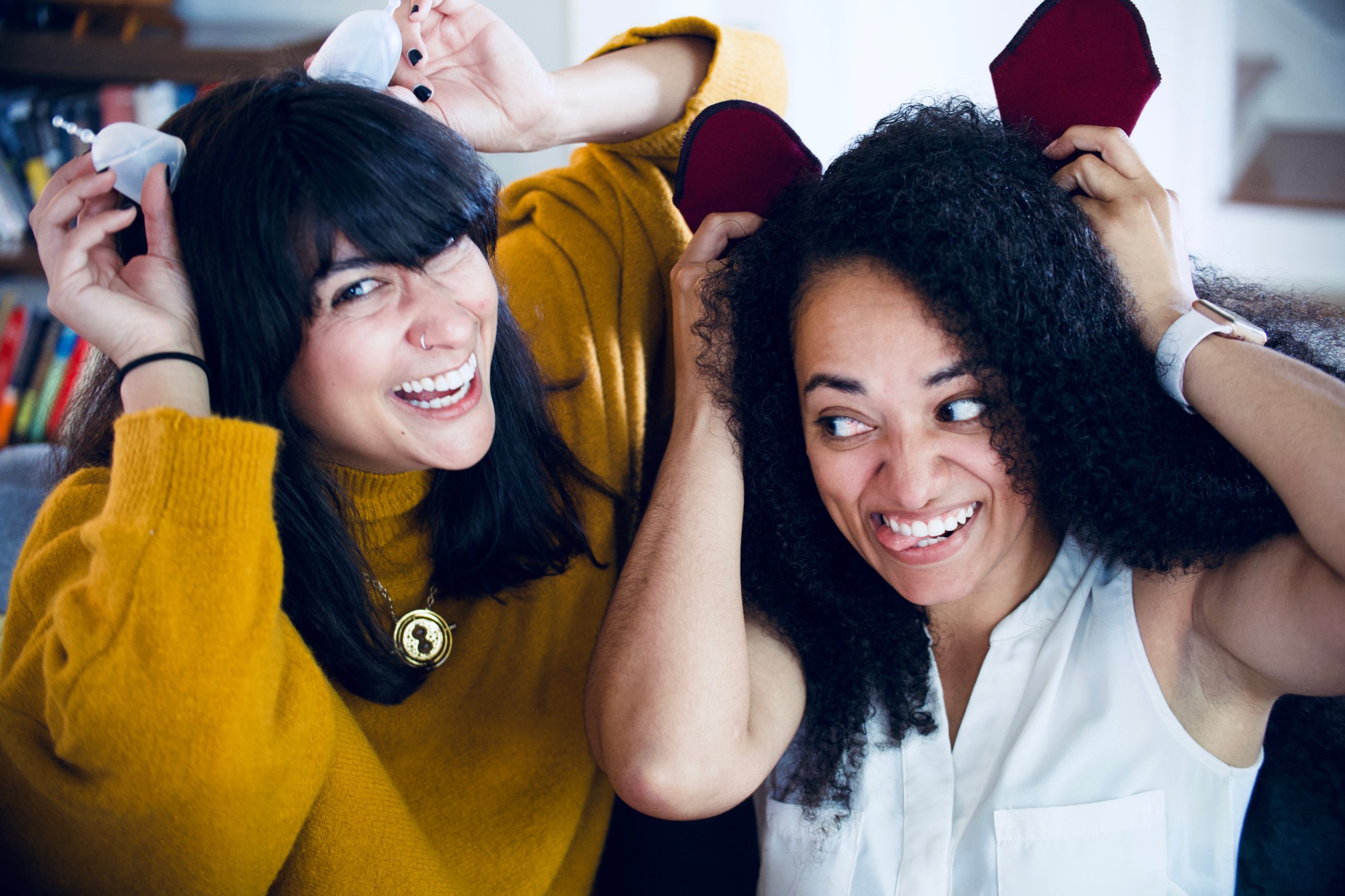 Two people act silly using menstrual cups and cloth pads as ears. 