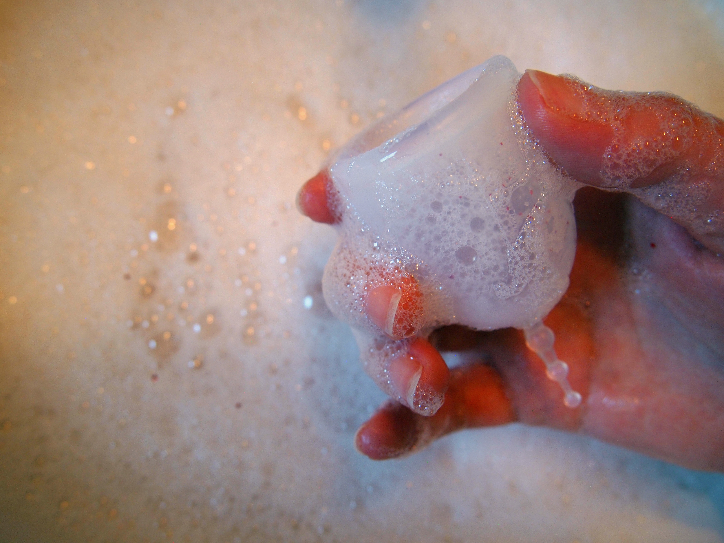 A person's hand holds a sudsy menstrual cup.