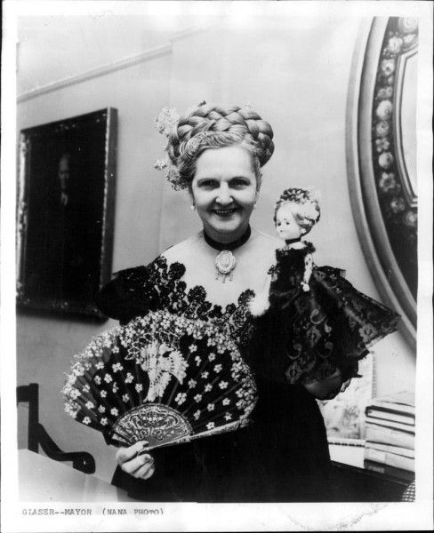 A black and white photo of Felisa Rincón de Gautier holding a fancy doll and a handheld fan. 