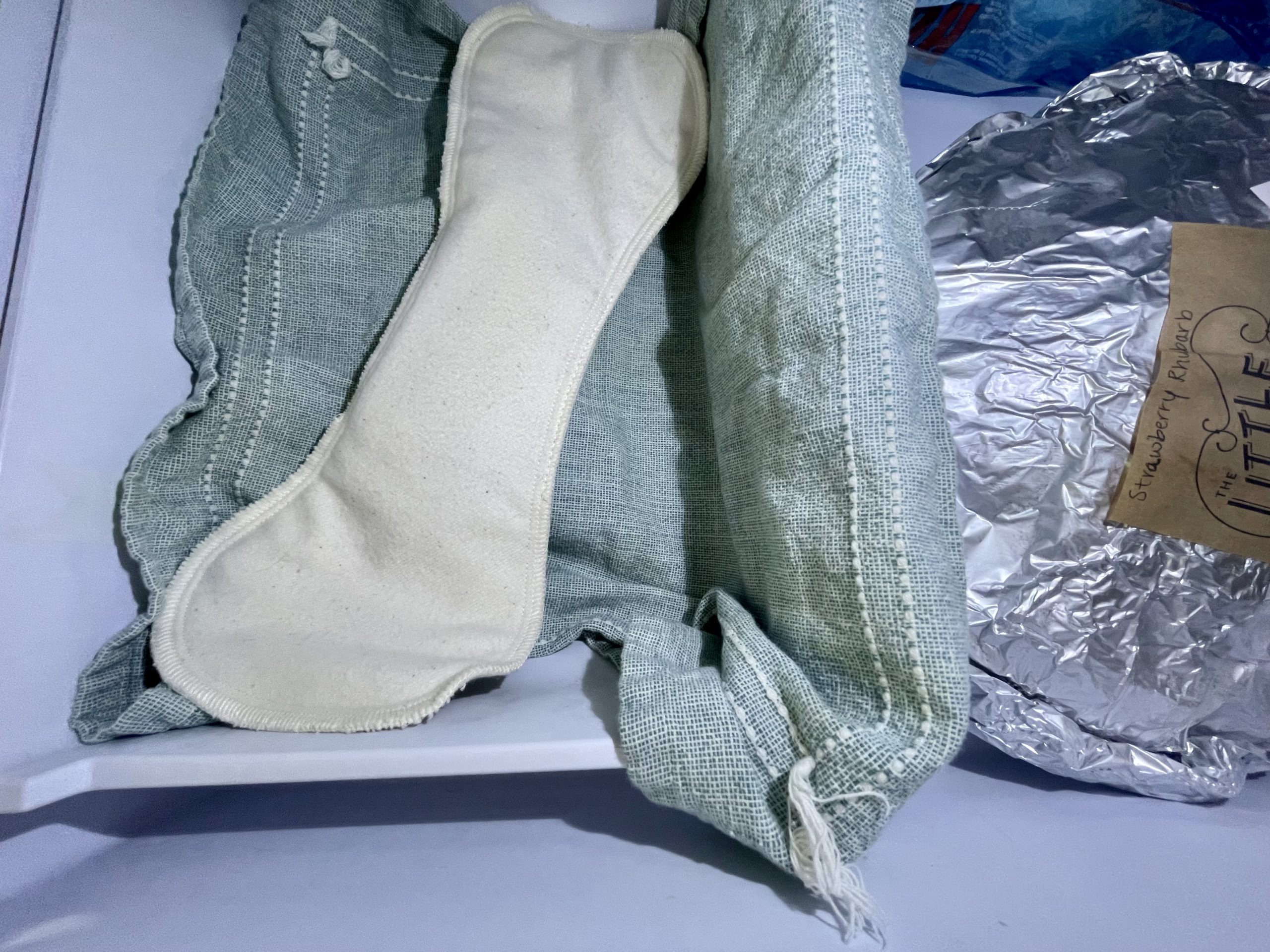 An organic overnight cloth pad sits on top of a cloth dishtowel inside a freezer drawer.