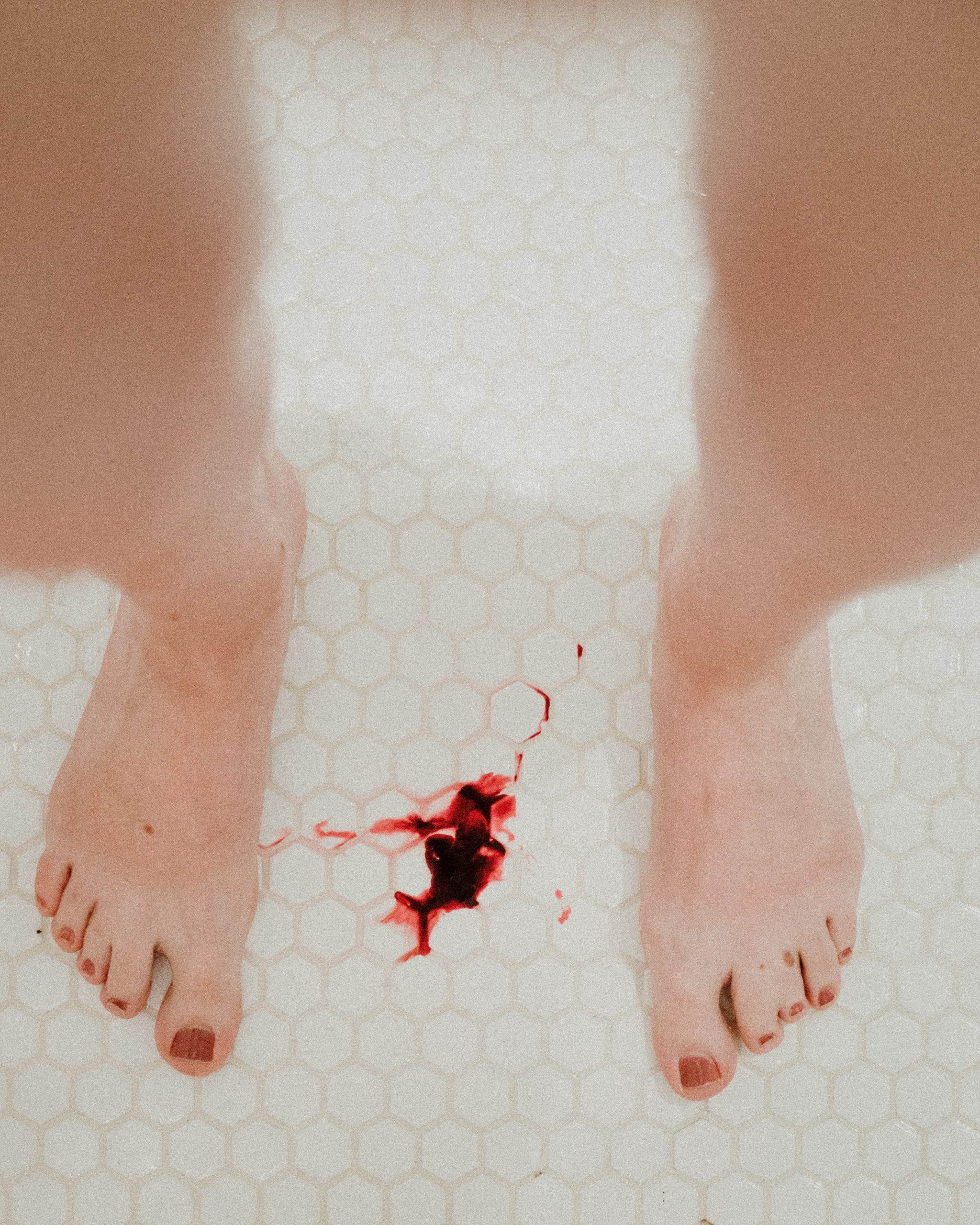 A person's bare feet on a tiled floor with a splash of blood on the tiles.